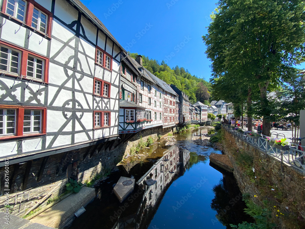 Monschau, Germany (Eifel) - July 9. 2020: View on river with timber frame monument houses in center of medieval village (focus on left house)