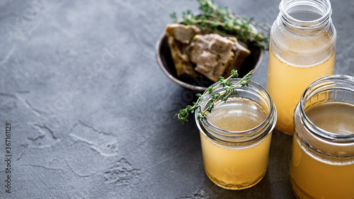 Glass jar with yellow fresh bone broth on dark gray background. Healthy low-calories food is rich in vitamins, collagen and anti-inflammatory amino acidsh