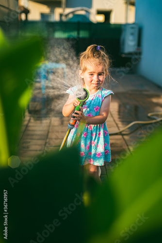 Happy 2-3 year old girl with garden hose water the plants plants.
