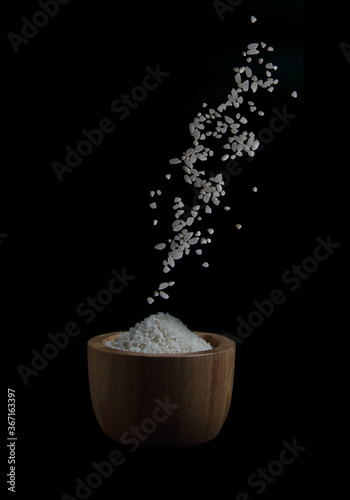rice pouring into wooden bowl on black background