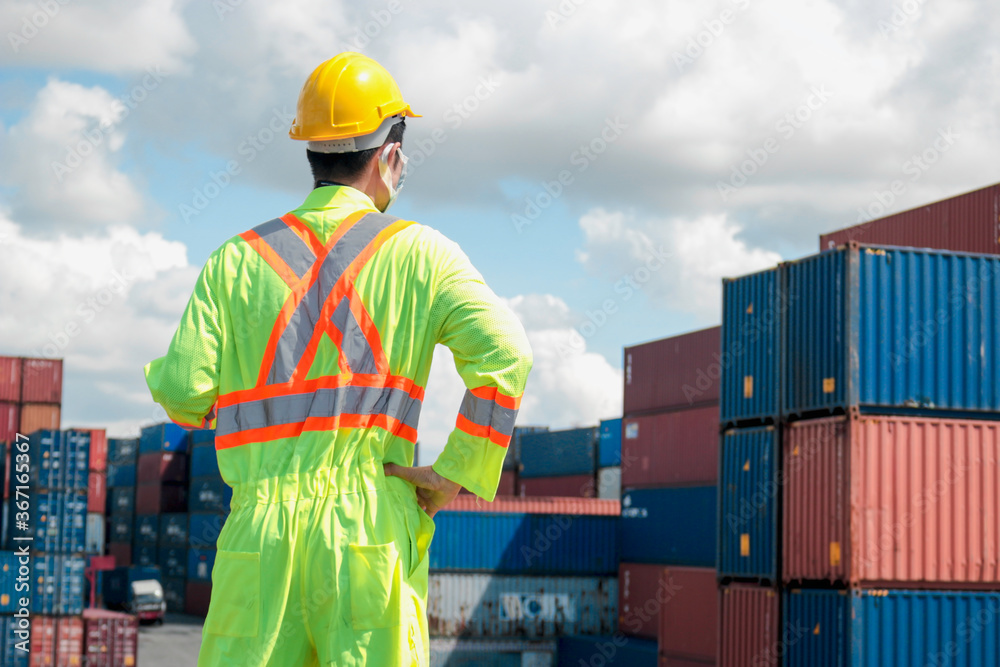 The back of worker man wearing safety clothing with helmet standing at logistic cargo containers shipping yard The back of worker man wearing safety clothing with helmet standing at logistic cargo containers shipping yard
