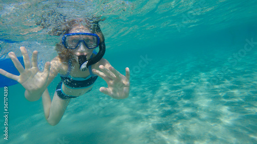 A girl snorkeling in the turquoise sea water and looking at camera.