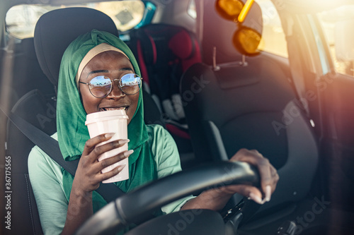 Arabian businesswoman wearing hijab, drinking coffee to go and driving her car. Middle eastern ethnicity woman in car as driver. Arabic woman in hijab driving a car photo