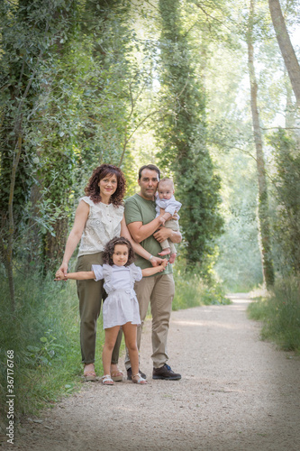 Family consisting of father mother baby and a girl posing in a grove surrounded by greenery.