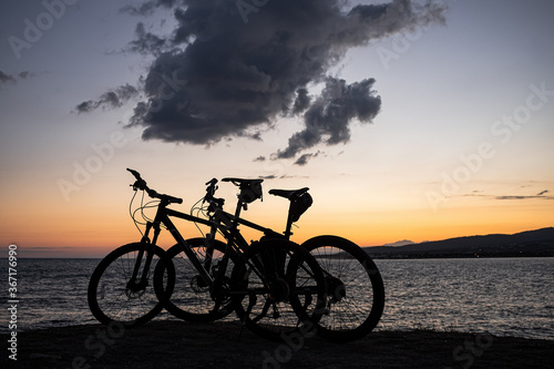 Two mountain bikes stand on the edge of a cliff, where you can see a bright orange sea sunset, mountains and large clouds. Recreation and sports in the resort city of Gelendzhik