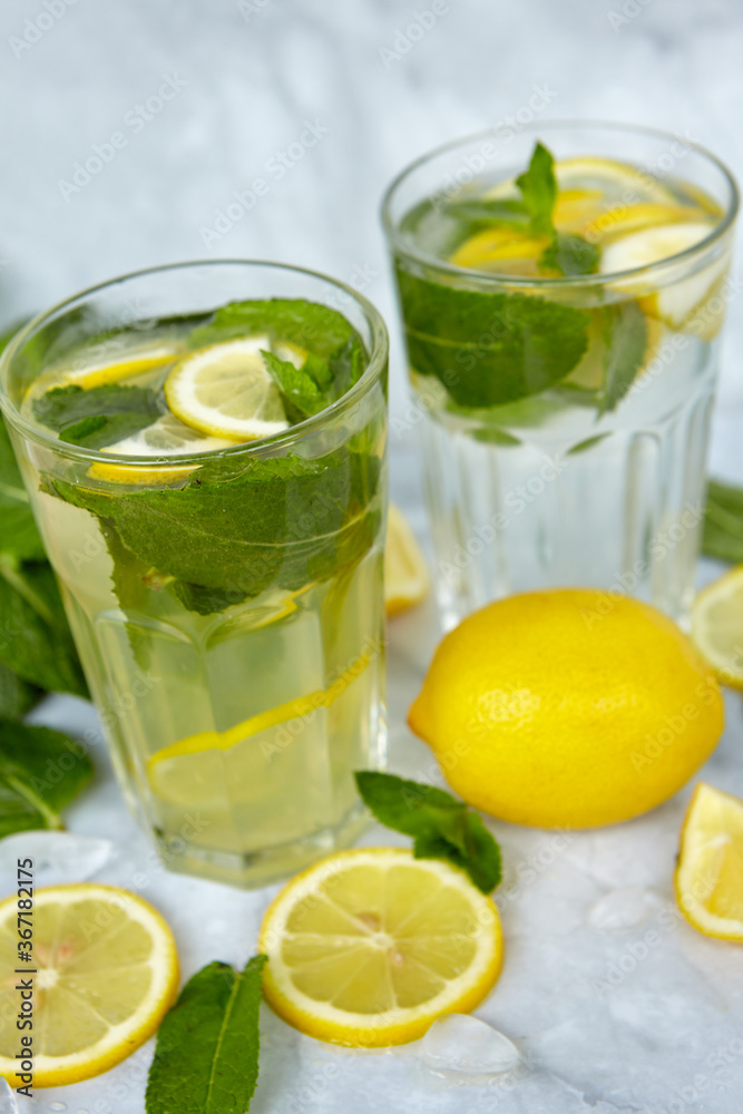 Refreshing drinks for summer, cold sweet and sour lemonade juice in the glasses with sliced fresh lemons. Refreshing summer drink. Traditional lemonade with lemon, mint and ice. Selective focus Refreshing drinks for summer, cold sweet and sour lemonade juice in the glasses with sliced fresh lemons. Refreshing summer drink. Traditional lemonade with lemon, mint and ice. Selective focus