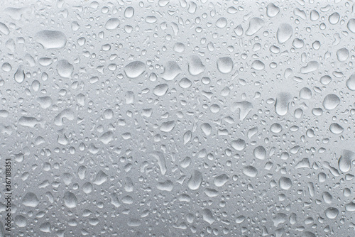 Drops of rain on the grey metallic surface of a car. Background with rain drops