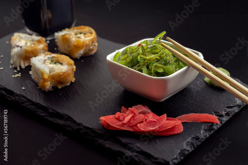 Sushi with eel and hayash wakamei salad lie on a black board made of stone slate