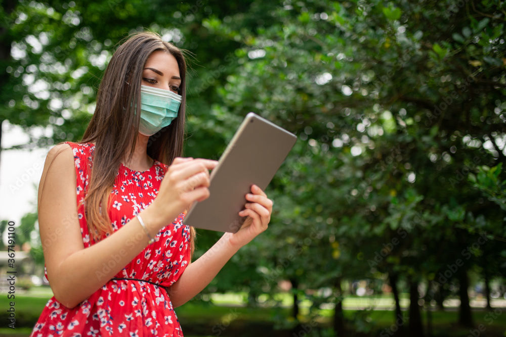 Masked woman using a tablet in the park Masked woman using a tablet in the park