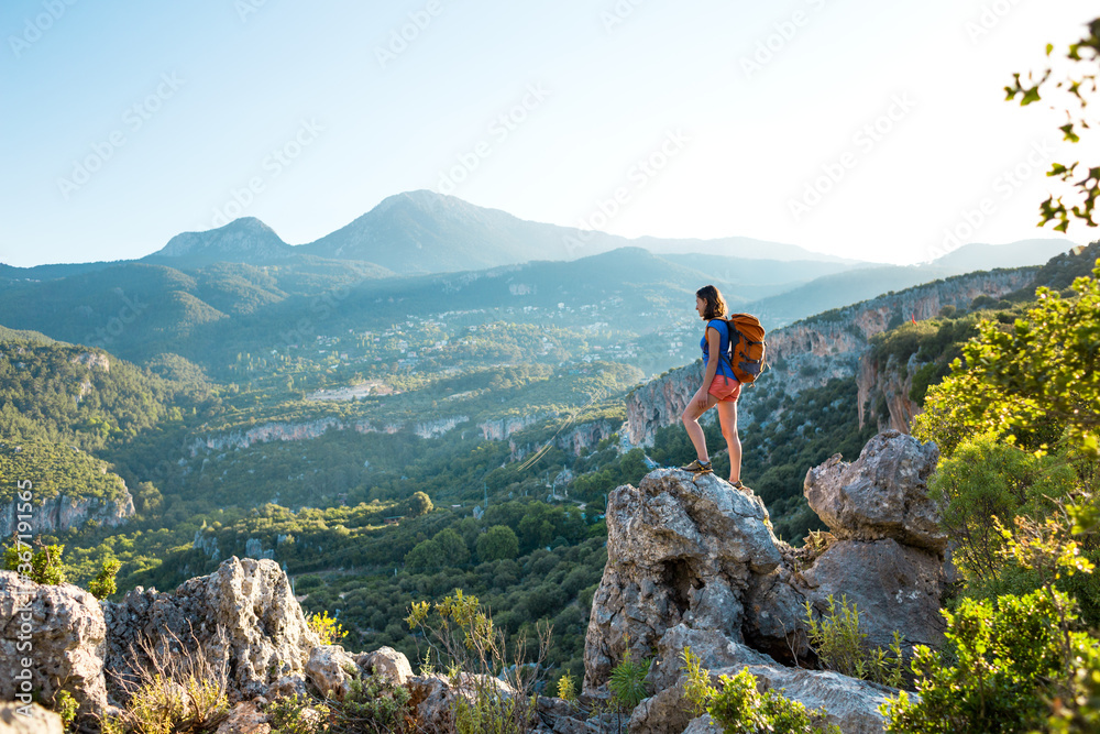 A woman with a backpack stands on top of a mountain and admires the beauty of a mountain valley.