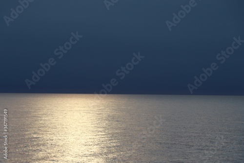 Φωτογραφία Beach area under a darkened sky with a glistening light on the stillness of the