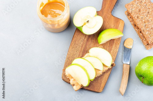 Making healthy sandwich with low carb whole grain cracker, green apple slices and peanut butter, on wooden board, horizontal, top view, copy space