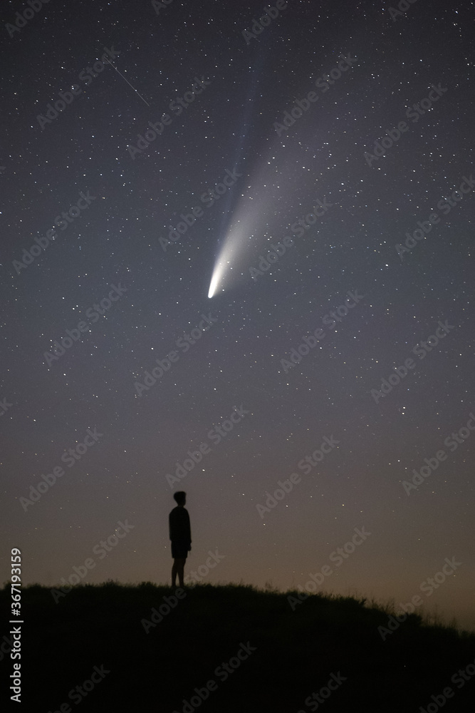 The dark silhouette of the young man is out of focus. Night starry sky and comet NEOWISE. Summer starry night. Beautiful night landscape. The dark silhouette of the young man is out of focus. Night starry sky and comet NEOWISE. Summer starry night. Beautiful night landscape.