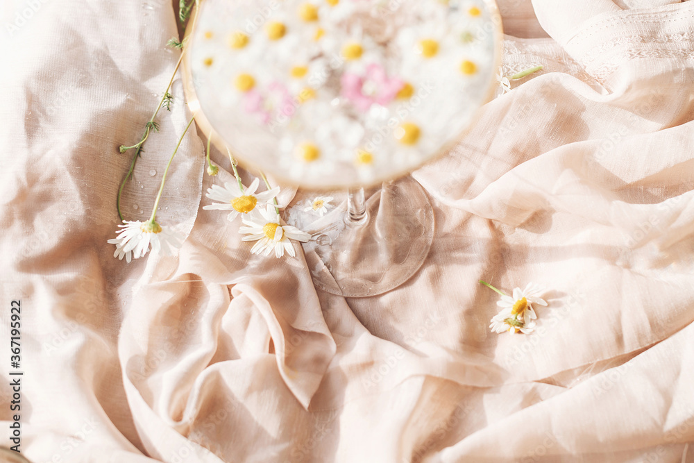 Daisy flowers at wineglass stem on background of soft beige fabric in sunny light. Tender floral aesthetic. Creative summer image. Bohemian mood Daisy flowers at wineglass stem on background of soft beige fabric in sunny light. Tender floral aesthetic. Creative summer image. Bohemian mood