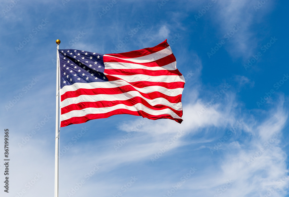 Bright American flag waving in the wind, with vibrant red white and blue colors lit by the sun, against blue sky for with copy space.