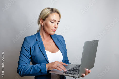 Blonde woman, long hair, in a blue jacket with a laptop in her hands, studio, light background