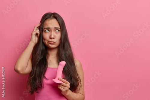 Obraz na plátně Indecisive Asian woman rubs head chooses dildo in sex shop holds silicone rosy p