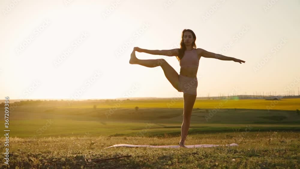 Young woman is practicing yoga outdoors in park evening on background beautiful field and sunset. Fitness and stretching in nature. Health and wellness. Sport Motivation. Slow motion