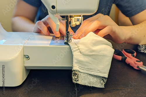 Woman sewing COVID-19 mask at home using sewing machine