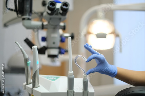 Fotografi Hand in Blue latex glove and saliva ejector in shape of heart and dental microsc