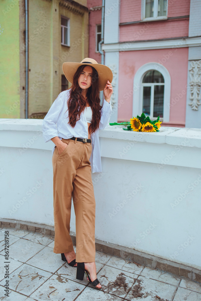 Young happy beautiful girl is walking in a shirt and pants with a bouquet of flowers of sunflowers on a city street