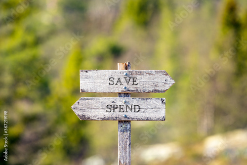 save spend text carved on wooden signpost outdoors in nature. Green soft forest bokeh in the background.