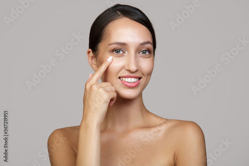 Canvas Print A young woman with a beautiful smile and teeth points her finger at her eyes