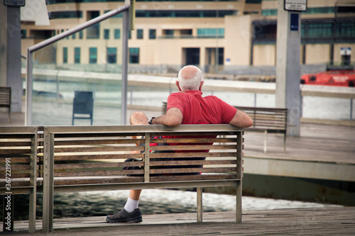 Elderly man sitting alone on a bench enjoying the day near a port