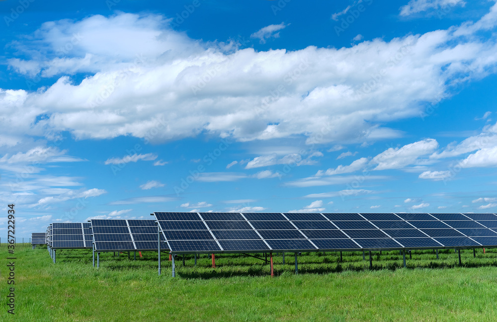 Solar power plant, blue solar panels on grass field under blue sky with clouds Solar power plant, blue solar panels on grass field under blue sky with clouds