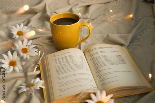 cup with black coffee, yellow open book, daisies and warm lights
