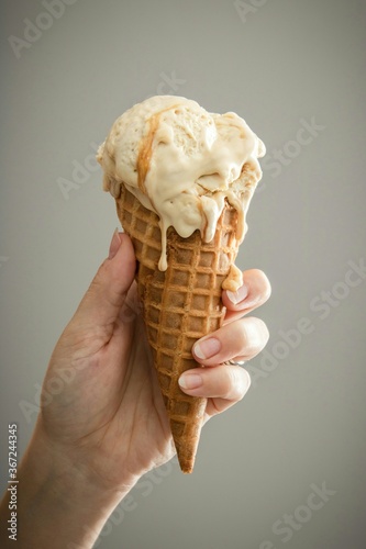 Women's hand holding a waffel ice cream cone with vanilla flavour.