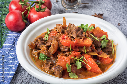 Veal stewed with vegetables in tomato sauce on a black concrete or stone background.
