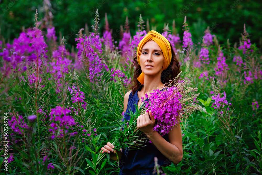 A young beautiful girl collects flowers in a field. A woman walks through a field of flowers. A bouquet of pink flowers of narrow-leaved cypress Ivan tea. A young beautiful girl collects flowers in a field. A woman walks through a field of flowers. A bouquet of pink flowers of narrow-leaved cypress Ivan tea.