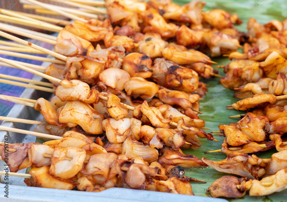 Squid skewers waiting to be grilled in charcoal grill. Thai delicious street food in local market.