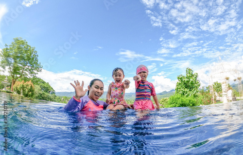 Asian sibling sisters playing in swimming pool with family in a hot summer day. Family lifestyle in vacation.