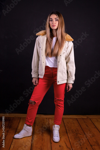 A young girl in a jacket and red trousers isolated on a black background
