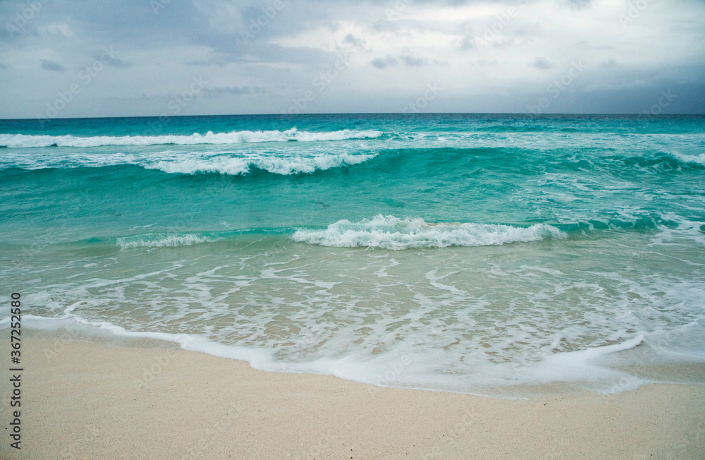 Magical beach seascape in the Caribbean. Beautiful view of the turquoise color sea water ocean. The white sand and ocean waves under a cloudy sky in Cancun, Mexico.  