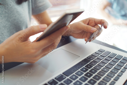 Female hands holding smart phone and credit card. Laptop computer on working desk. Shopping and online payment by using notebook.