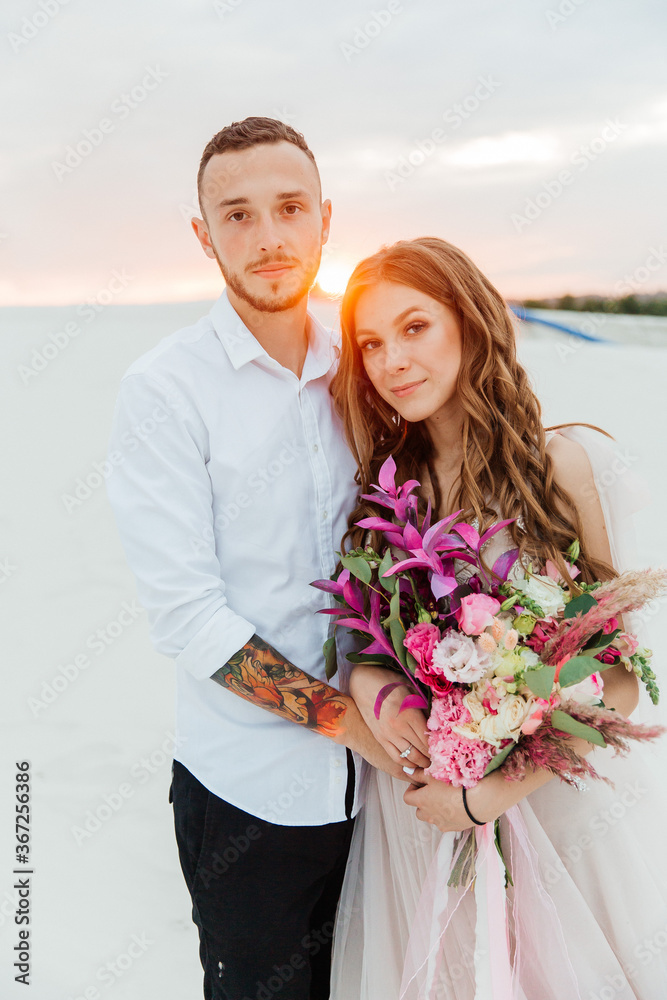 Love Story of a beautiful couple in a pink wedding luxury dress with a bouquet in the Sahara desert, sand, dunes Love Story of a beautiful couple in a pink wedding luxury dress with a bouquet in the Sahara desert, sand, dunes