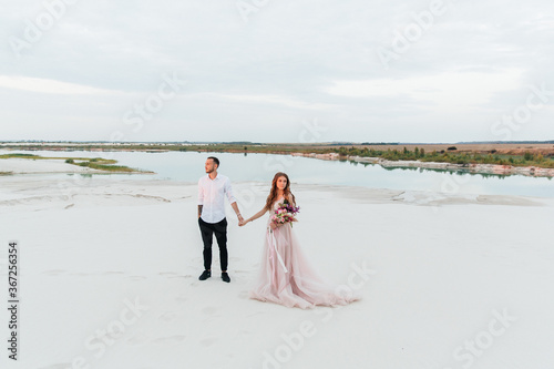 Love Story of a beautiful couple in a pink wedding luxury dress with a bouquet in the Sahara desert  sand  dunes
