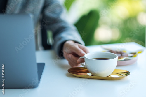 Closeup image of a business woman using and working on laptop computer while drinking coffee in office
