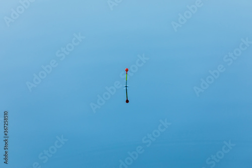 Tall fishing vivid or colorful float on the blue water surface of lake, river or pond in bright sunny day