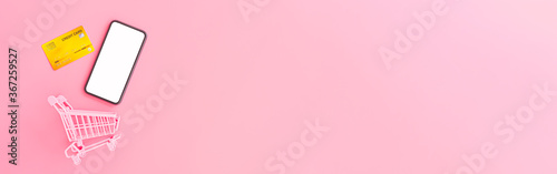 shopping and payment online concept from pink purse, credit cards, shopping cart and blank smartphone on pink pastel color background. web banner size.