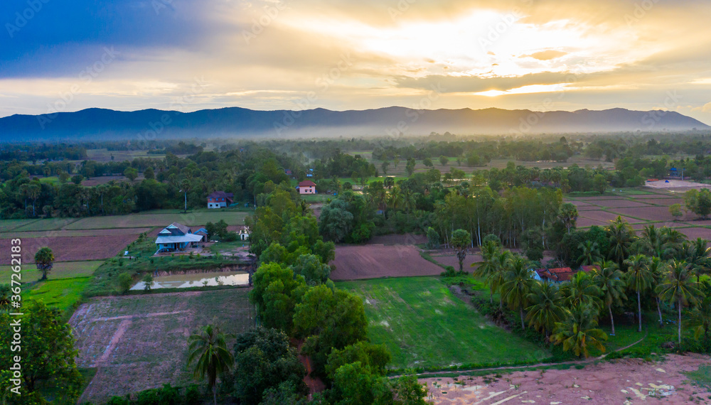 A top down aerial view of a small country town with traditional houses in Sunset besides mountain in Cambodia.