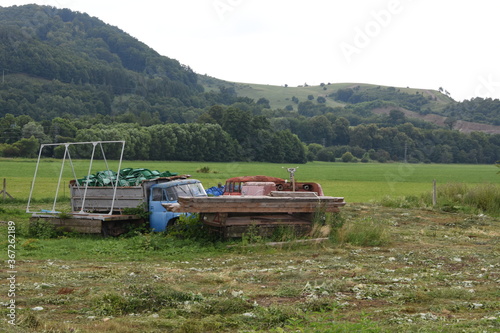 Wreck a goods carriage car full of plastic chairs and fire fighting truck. In the background highlands with green trees and bushes during summer day.