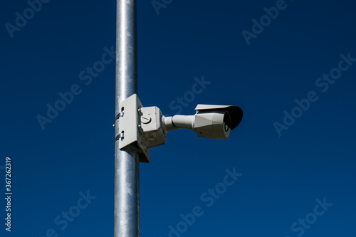 White security camera on metal pole against blue sky background