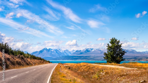 Panoramic view from Mount Cook Highway at Lake Pukaki, one of the most spectacular alpine scenery in the world in New Zealand, South Island, on a summer day with snow-capped mountains in background.
