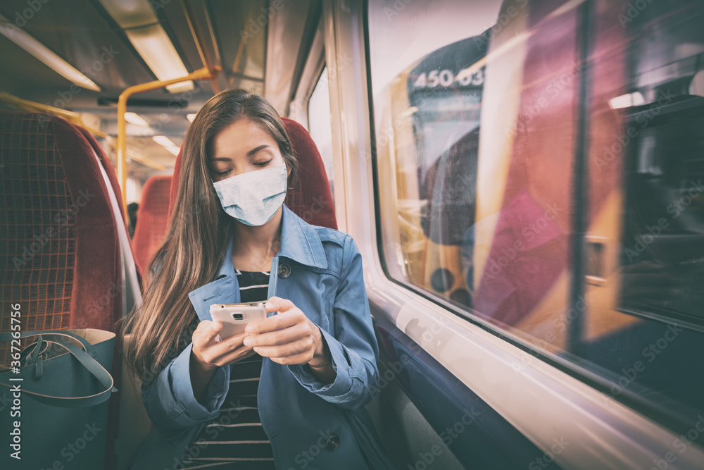 Mask wearing mandatory inside public spaces for transport such as train station and bus. Asian woman passenger using mobile phone with face covering wear sitting indoors on commute. - obrazy, fototapety, plakaty 