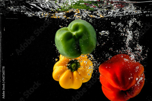 Three multi-colored colours Pepper splashing into water on black background photo