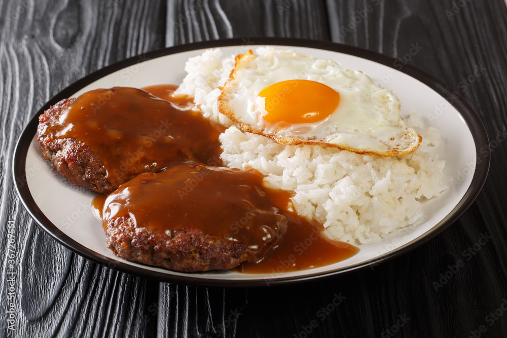 loco moco is a Hawaiian cuisine made with white rice with a hamburger patty, sunny side up egg, and brown beef gravy close-up on a plate. Horizontal loco moco is a Hawaiian cuisine made with white rice with a hamburger patty, sunny side up egg, and brown beef gravy close-up on a plate. Horizontal
